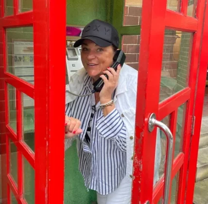 Silvi in roter klassischer alter englischer Telefonzelle mit Hoerer am Ohr